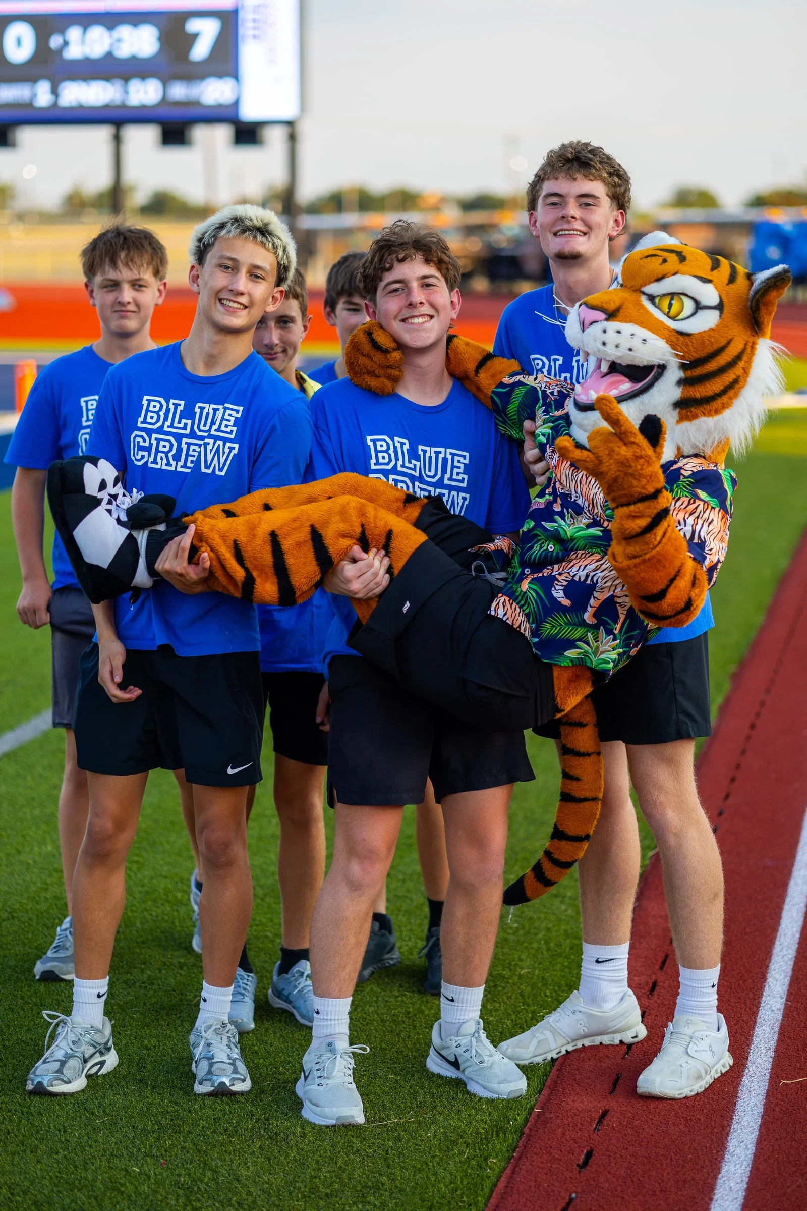 Five Wills Point Blue Crew students carrying the tiger mascot along the track before kickoff