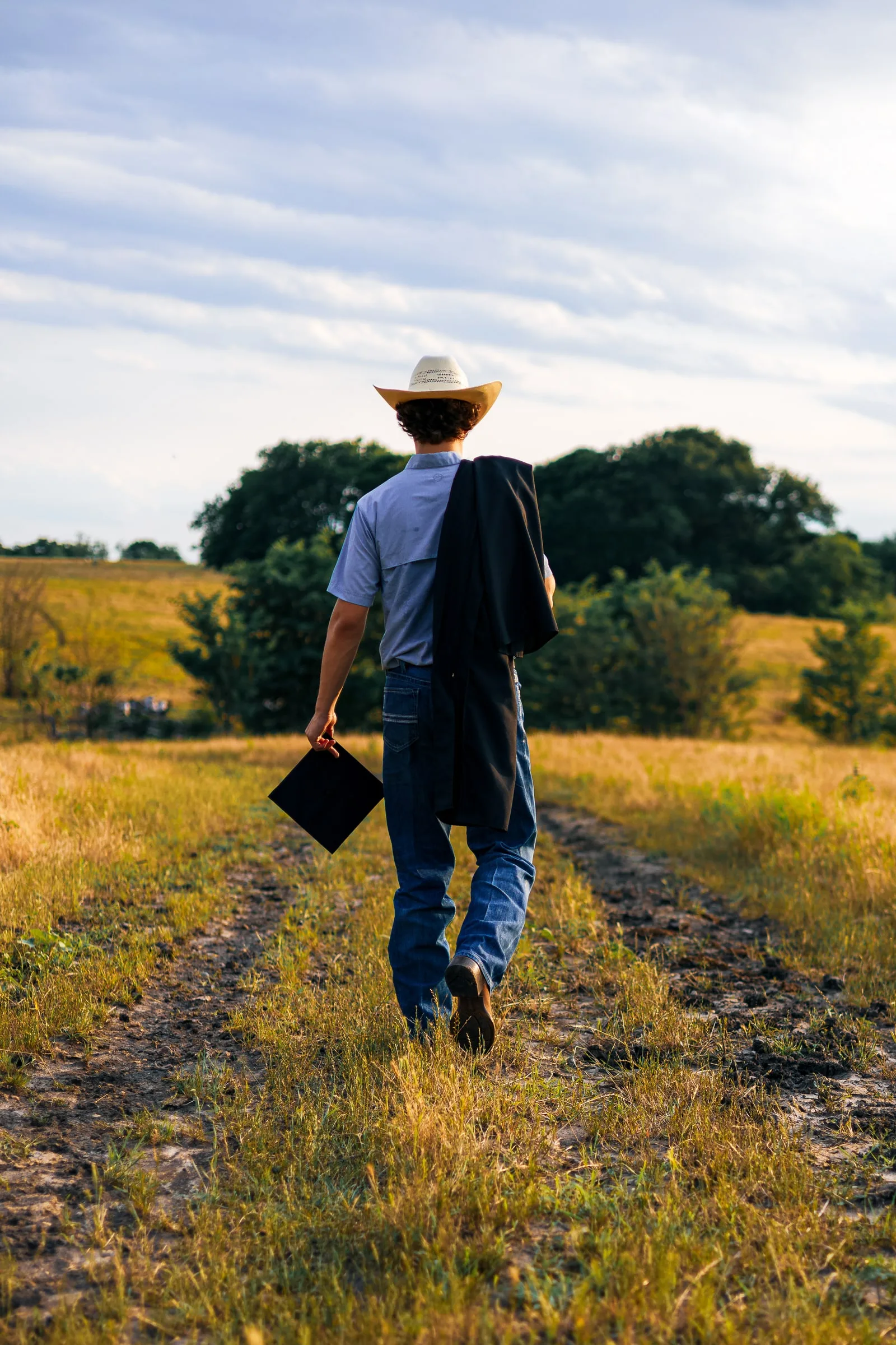 Graduate walking away down a field path carrying a cap and gown